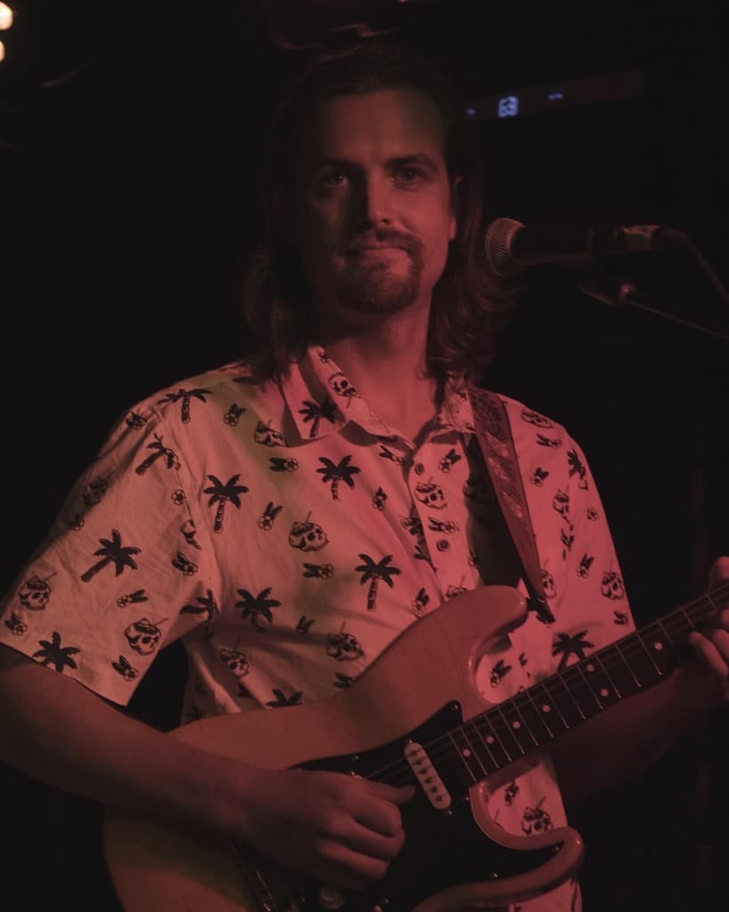 Luke Moore performing on electric guitar in palm shirt