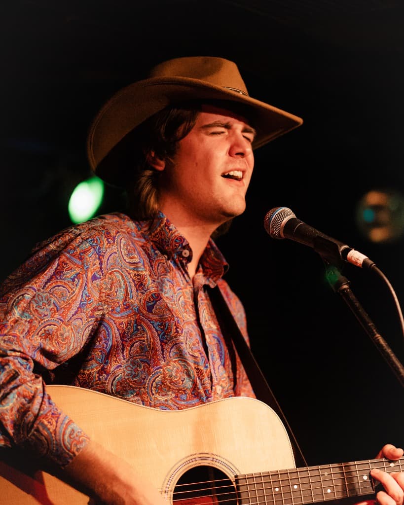 Luke Moore singing with vintage acoustic guitar in warm lighting